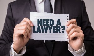 Man in suit holding sign with text 'Need a lawyer?'