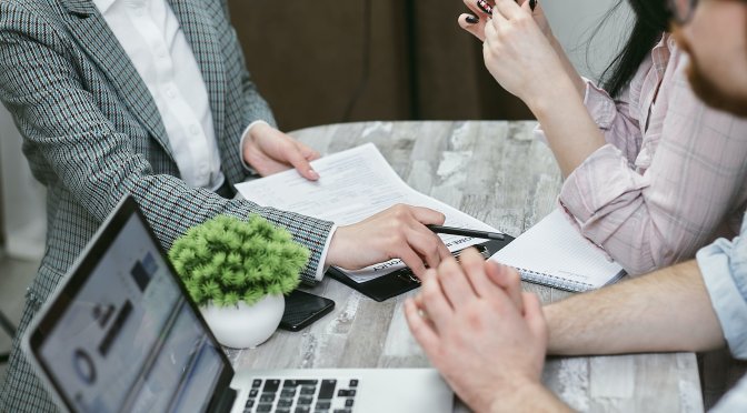 three people speaking at a table with laptop and paperwork in front of them