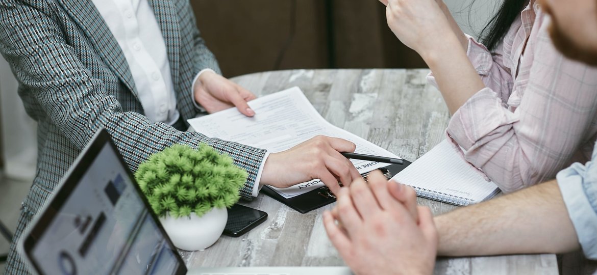 three people speaking at a table with laptop and paperwork in front of them
