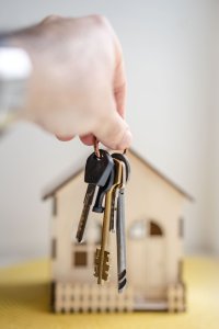 Hand with keys in front of wooden miniature house