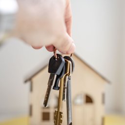 Hand with keys in front of wooden miniature house