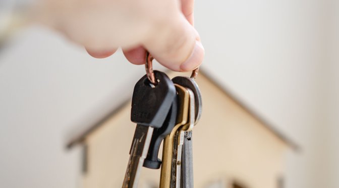 Hand with keys in front of wooden miniature house