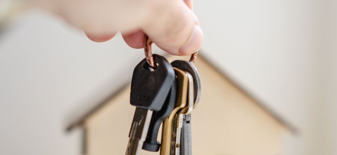 Hand with keys in front of wooden miniature house