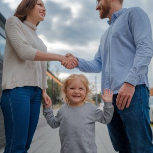 Co-parents shanking hands with a little girl smiling between them